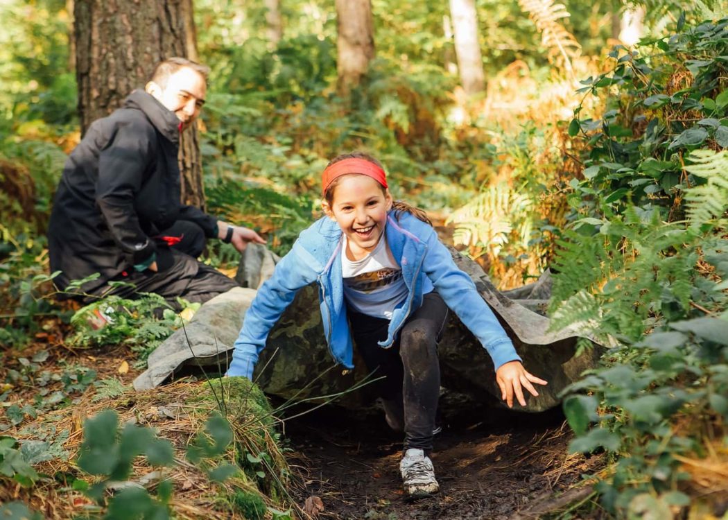 Child scrambles over a log at our Outdoor Learning "Academy of Danger" PE session in Greno Woods.