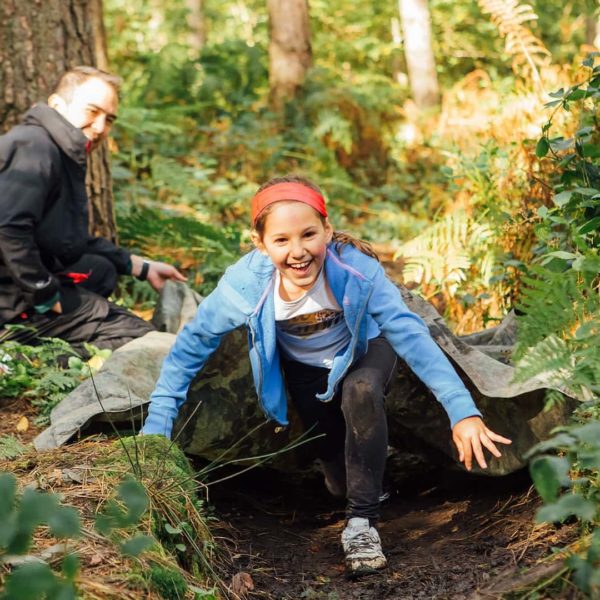 Child scrambles over a log at our Outdoor Learning "Academy of Danger" PE session in Greno Woods.