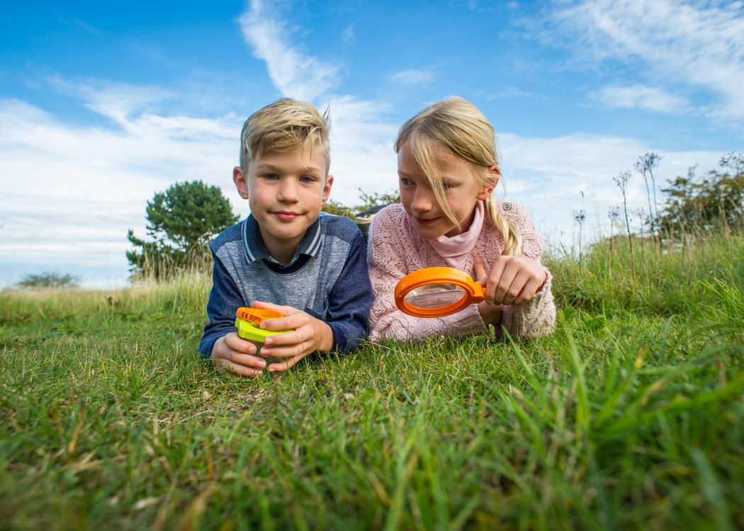 Nature Detectives - two choldren lying on grass with a magnifying glass