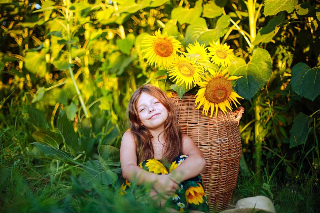 Young girl with red hair sits by a basket containing several tall sunflowers. © Photopashover / Envato Elements