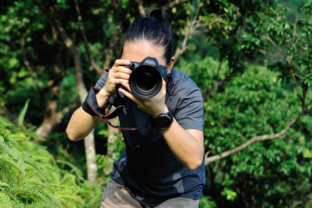 Young woman pointing a camera directly at the viewer whilst stood in a forest. © lzf / Envato Elements