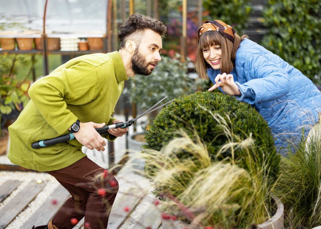 Young couple pruning round bush in their garden © RossHelen / Envato Elements