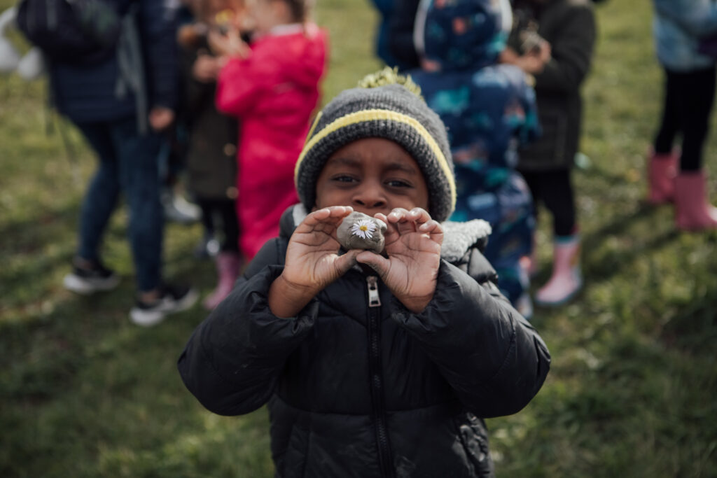 Young boy holding a stone to camera with a daisy stuck on it