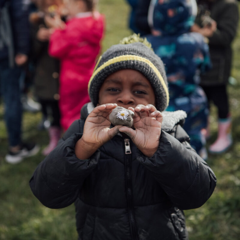 Young boy holding a stone to camera with a daisy stuck on it