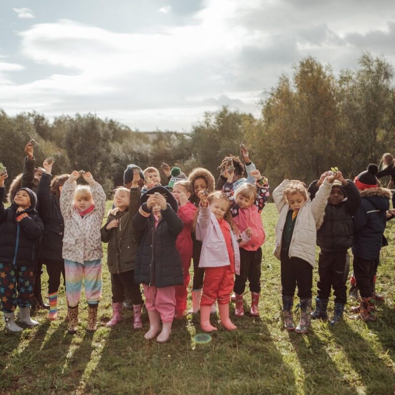 Group of children wearing outdoor clothes standing outside with their hands in the air