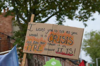 Sign reads 'I want you to act as you would in a crisis, act like our house is on fire - because it is!'