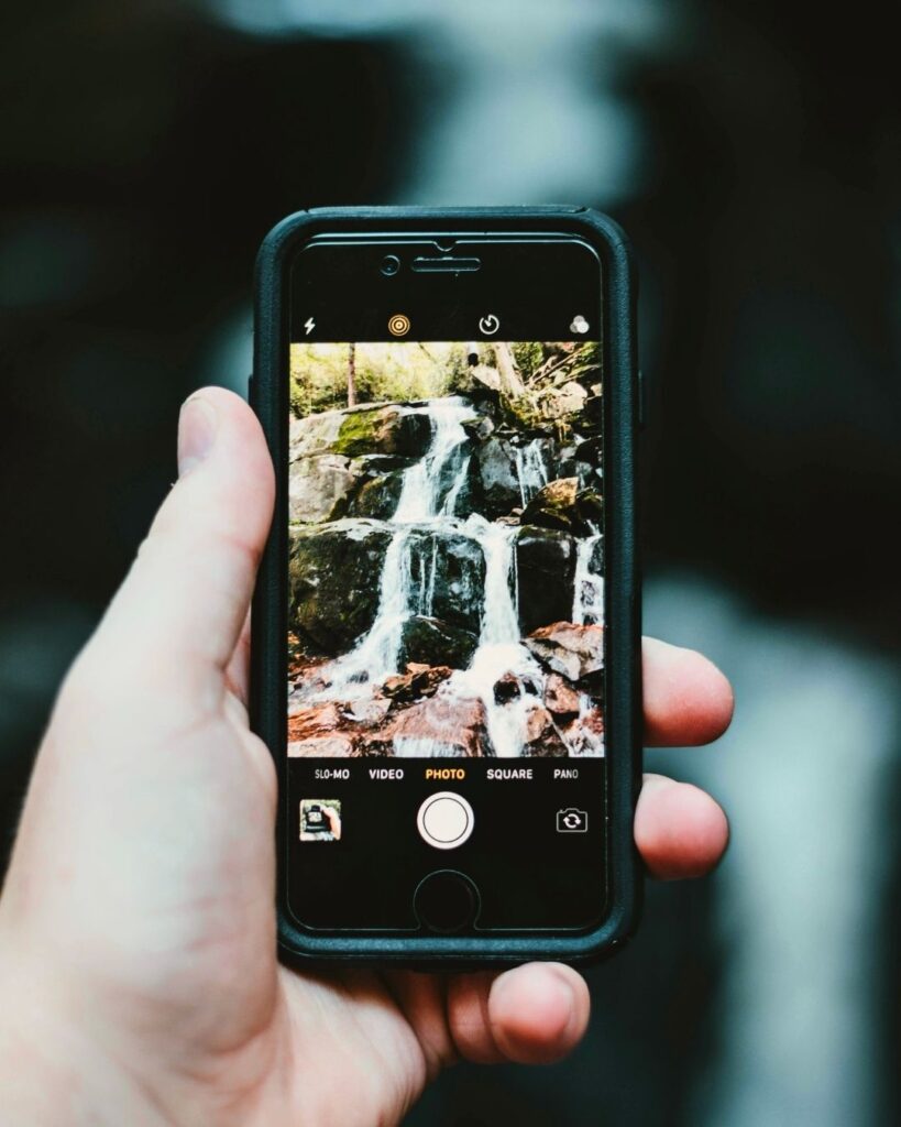 A hand holding a mobile phone taing a picture of a stream tumbling over rocks