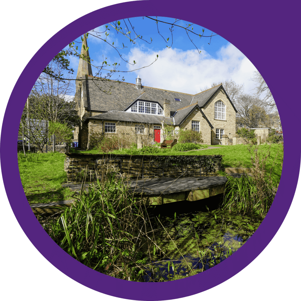 A view of Sheffield & Rotherham Wildlife Rrust's headquarters, where there is ofice space to rent. It is a sunny day with a blue sky and the photo is showing the wildlife garden and outdoor seating.