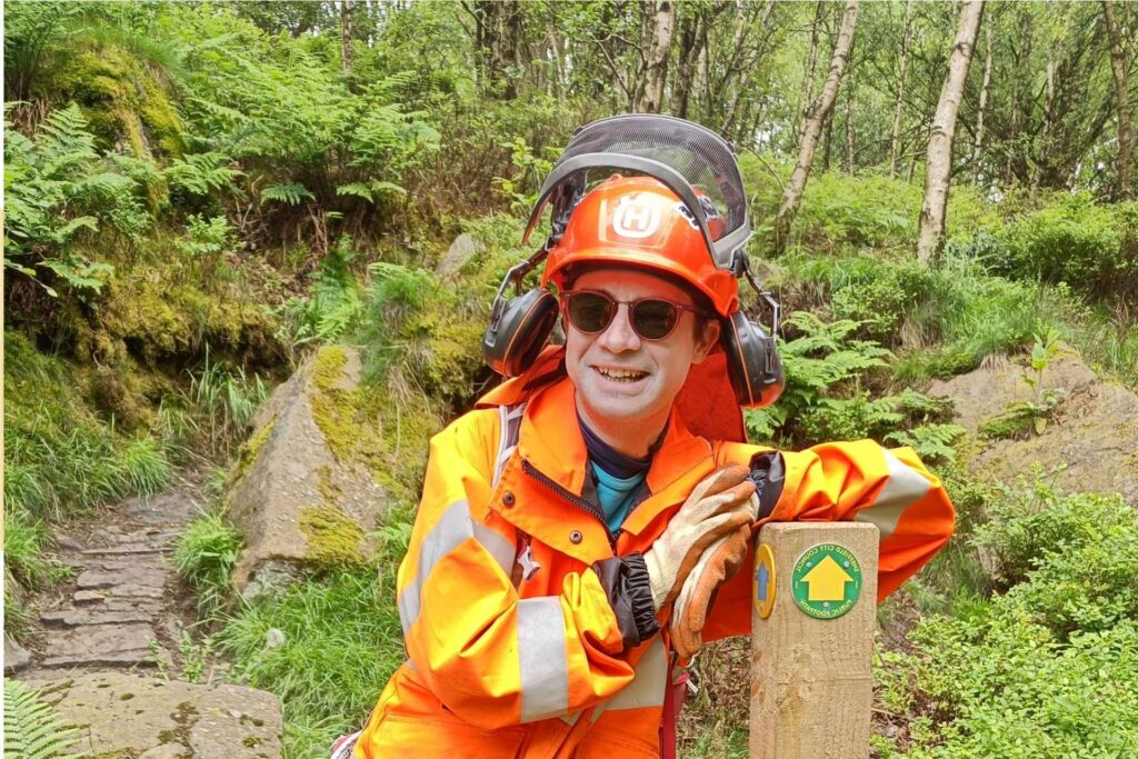 Volunteer jesse leans against a recently installed waymarker