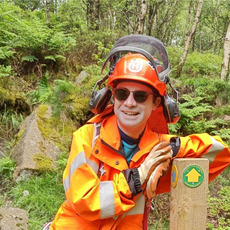 Volunteer jesse leans against a recently installed waymarker